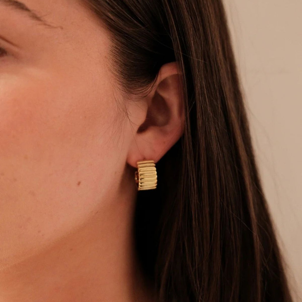 Close-up of a person wearing a gold hoop earring with a neutral background