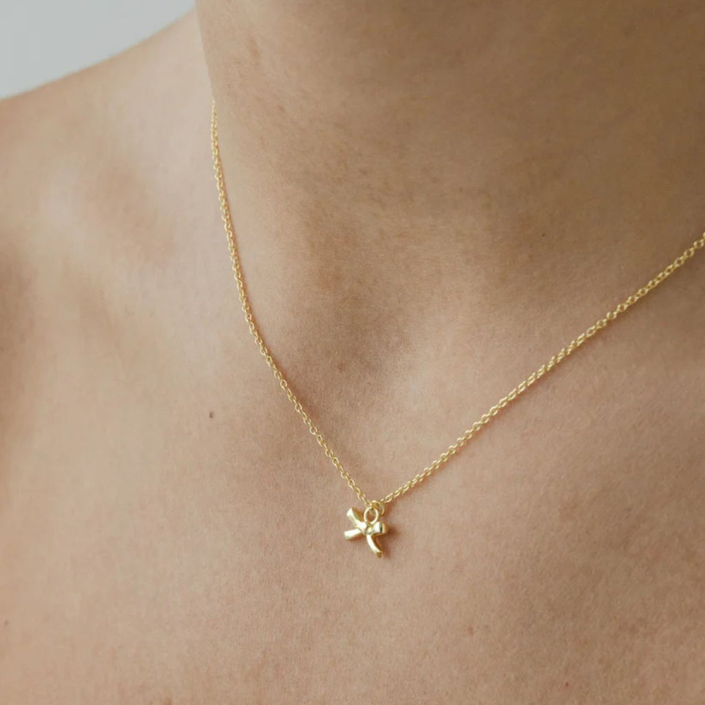 Gold necklace with a small pendant on a person's neck against a neutral background