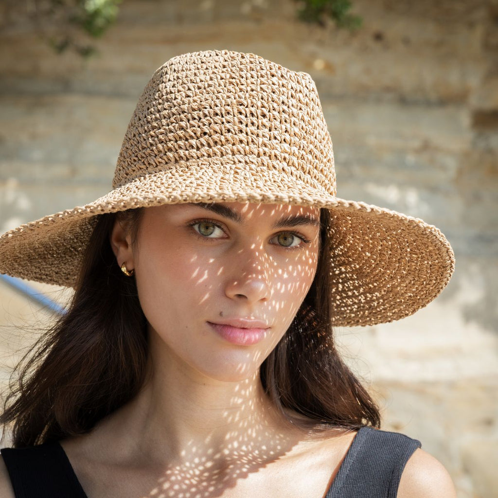 Woman wearing a straw hat with sunlight casting shadows on her face, against a stone wall background.