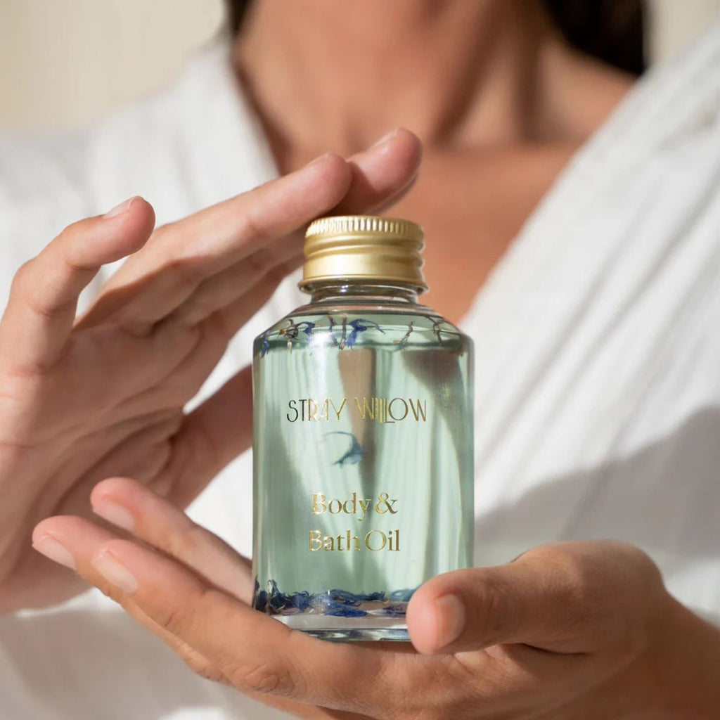 Person holding a bottle of Stray Willow body and bath oil with a gold cap.