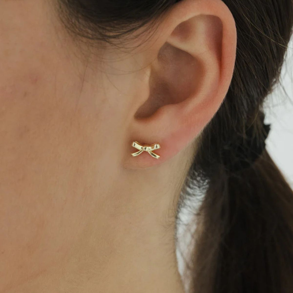 Gold bow-shaped earring worn on a person's ear.