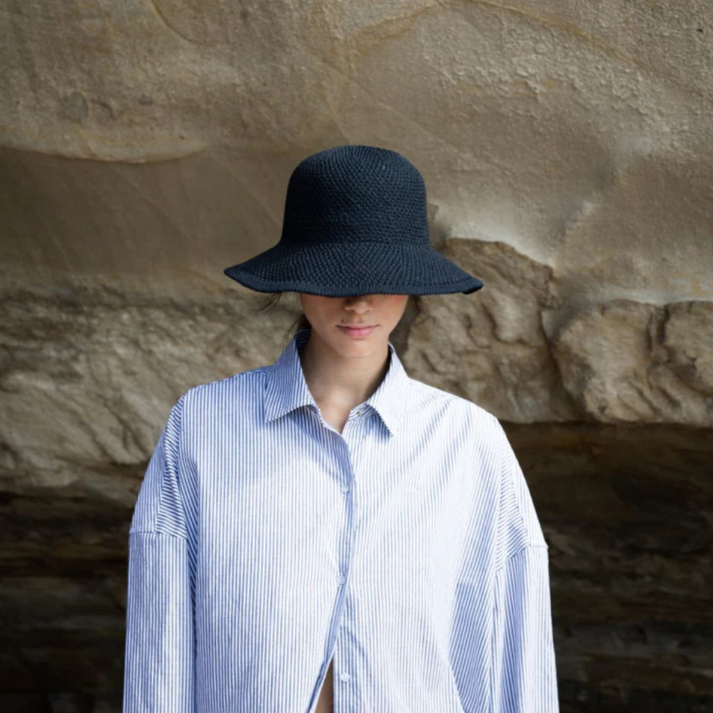 Person wearing a blue and white striped shirt and black hat against a stone wall.