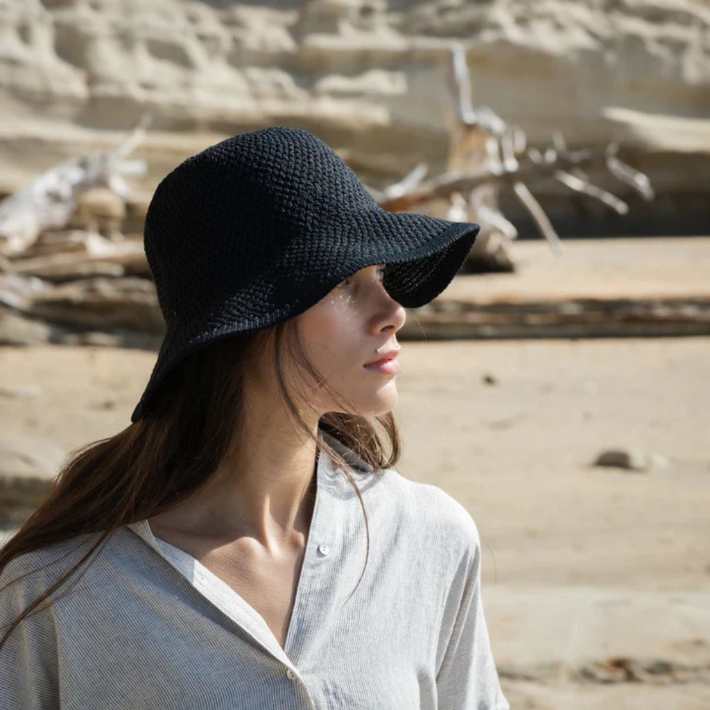 Woman wearing a black hat in a desert-like setting with sand and rocks.
