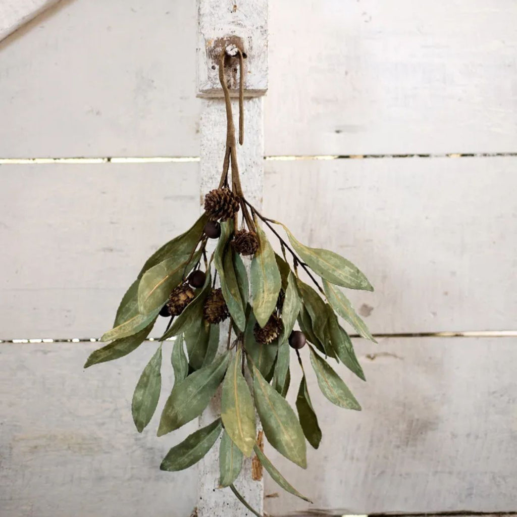Hanging green leafy branch with cones against a white wooden background