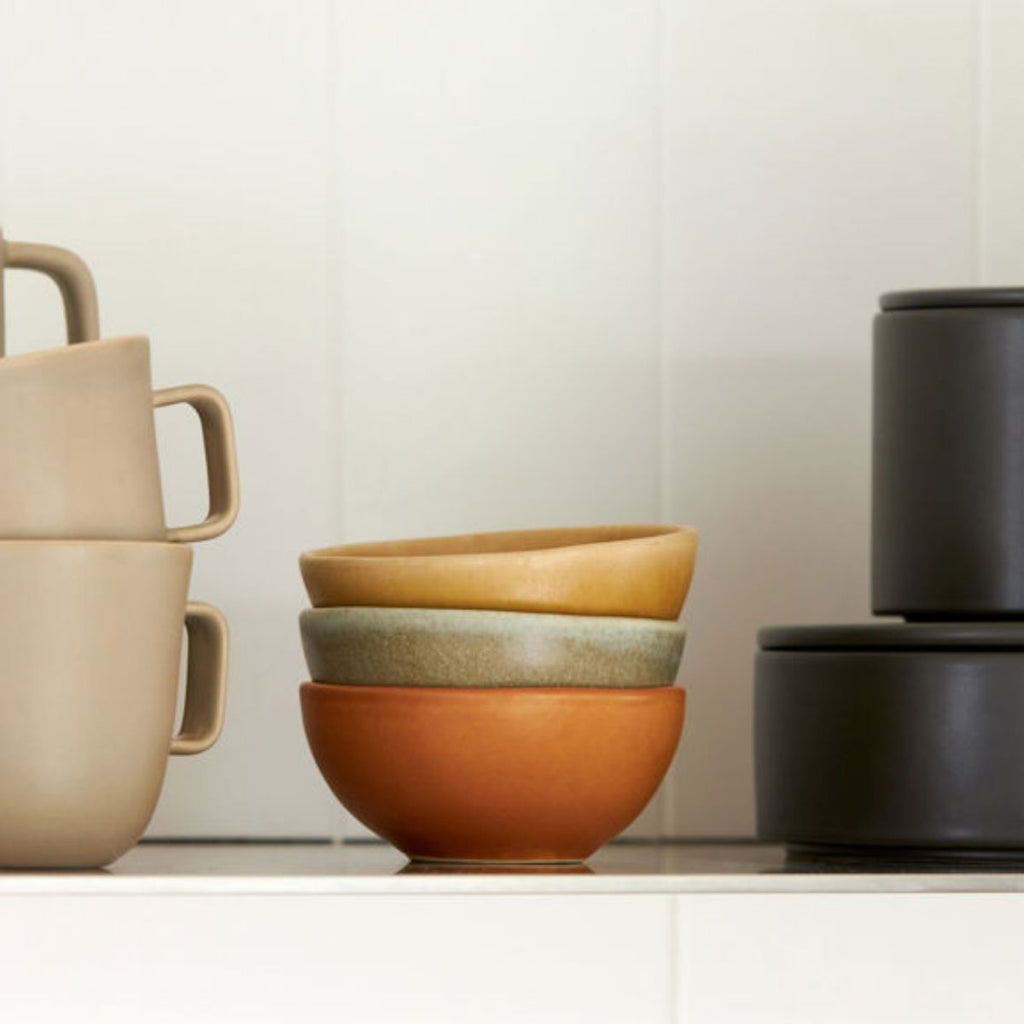 Set of ceramic bowls and mugs in various colors on a neutral background