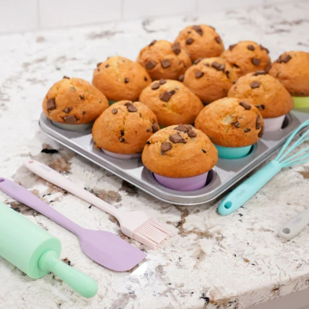 Muffins in a pan with colorful silicone baking tools on a marble surface