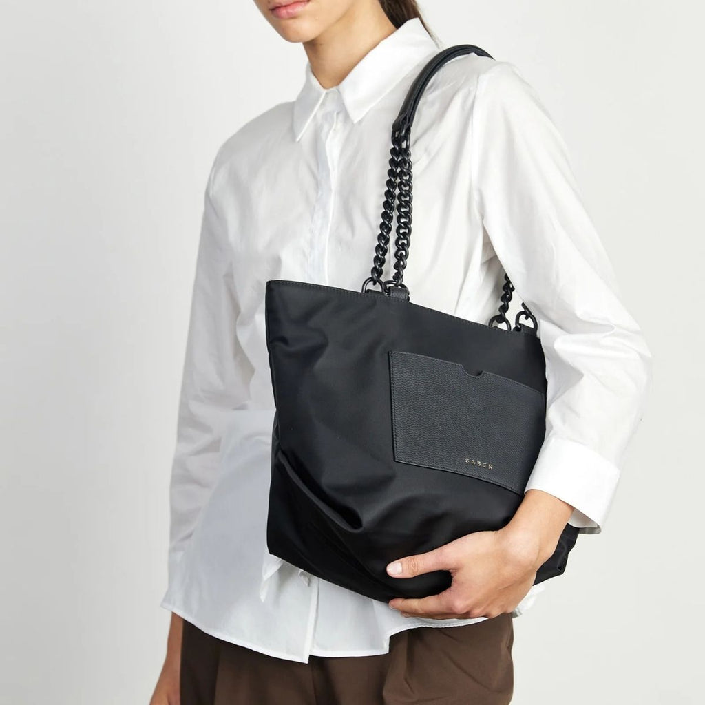Person holding a black handbag with a visible brand logo against a white background
