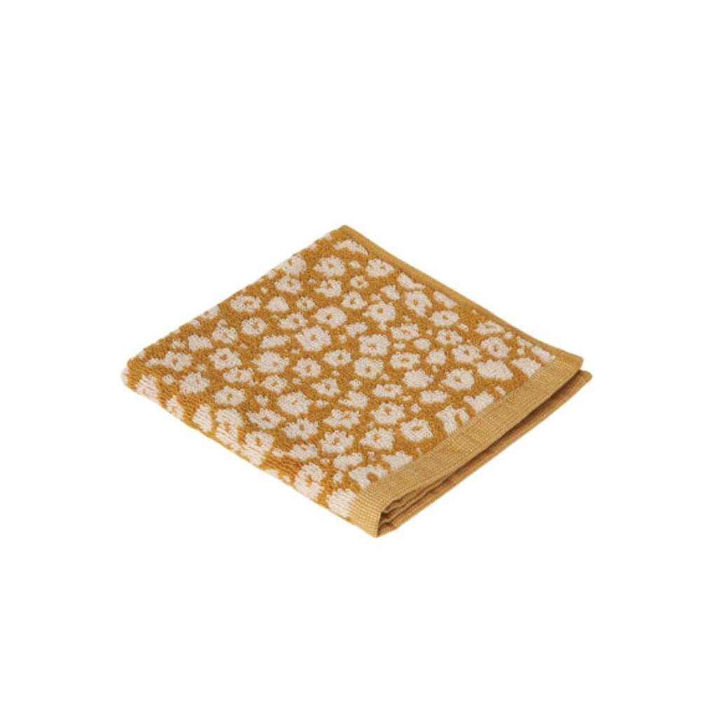 Folded mustard yellow facecloth with white floral pattern on a white background
