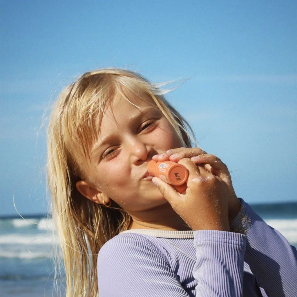 Young girl holding a orange lip balm against a clear blue sky