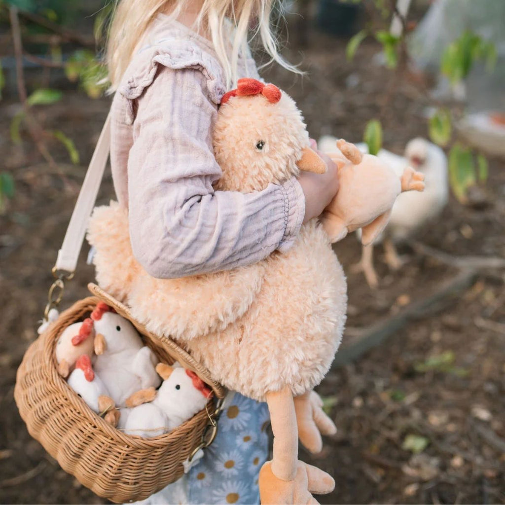 Child holding a fluffy toy with small stuffed animals in a basket, outdoors.