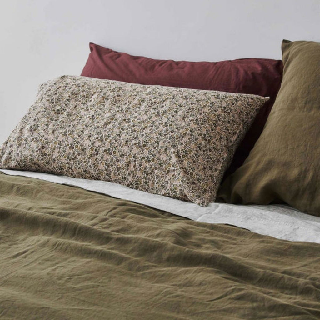 Bed with floral-patterned pillow, maroon pillow, and green pillow on a neutral background