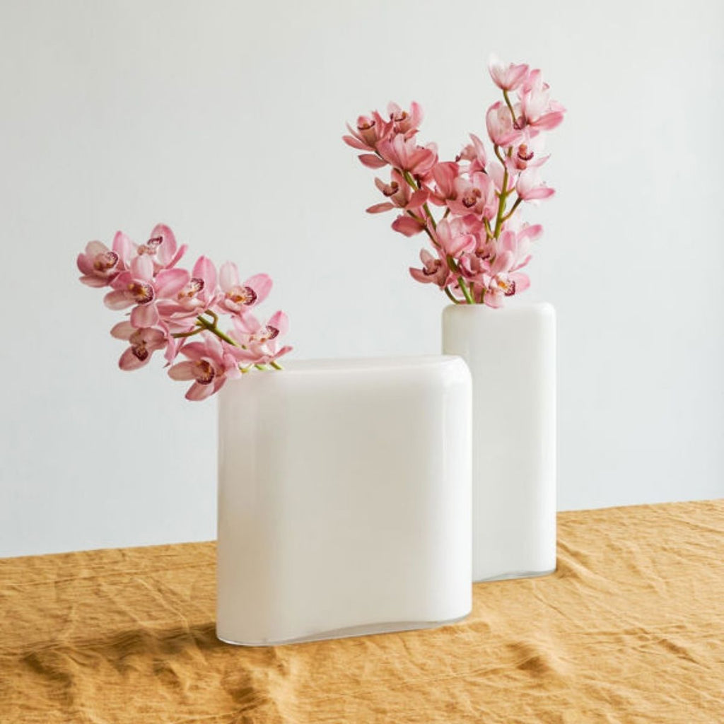 Two white vases with pink flowers on a wooden surface against a light background