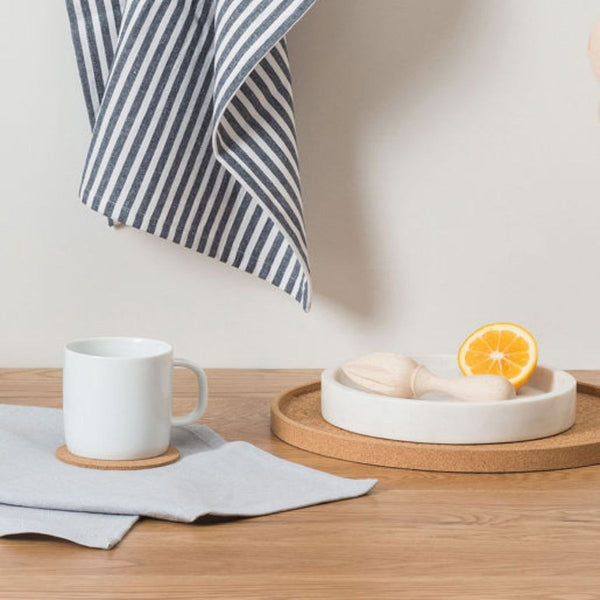 White mug on a wooden table with a striped towel and small dish with an orange slice.
