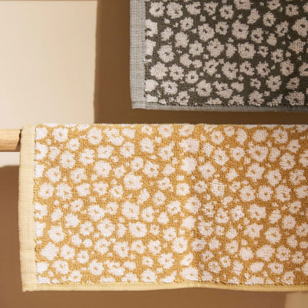 Two face cloths with floral patterns on a wooden rod against a beige background.