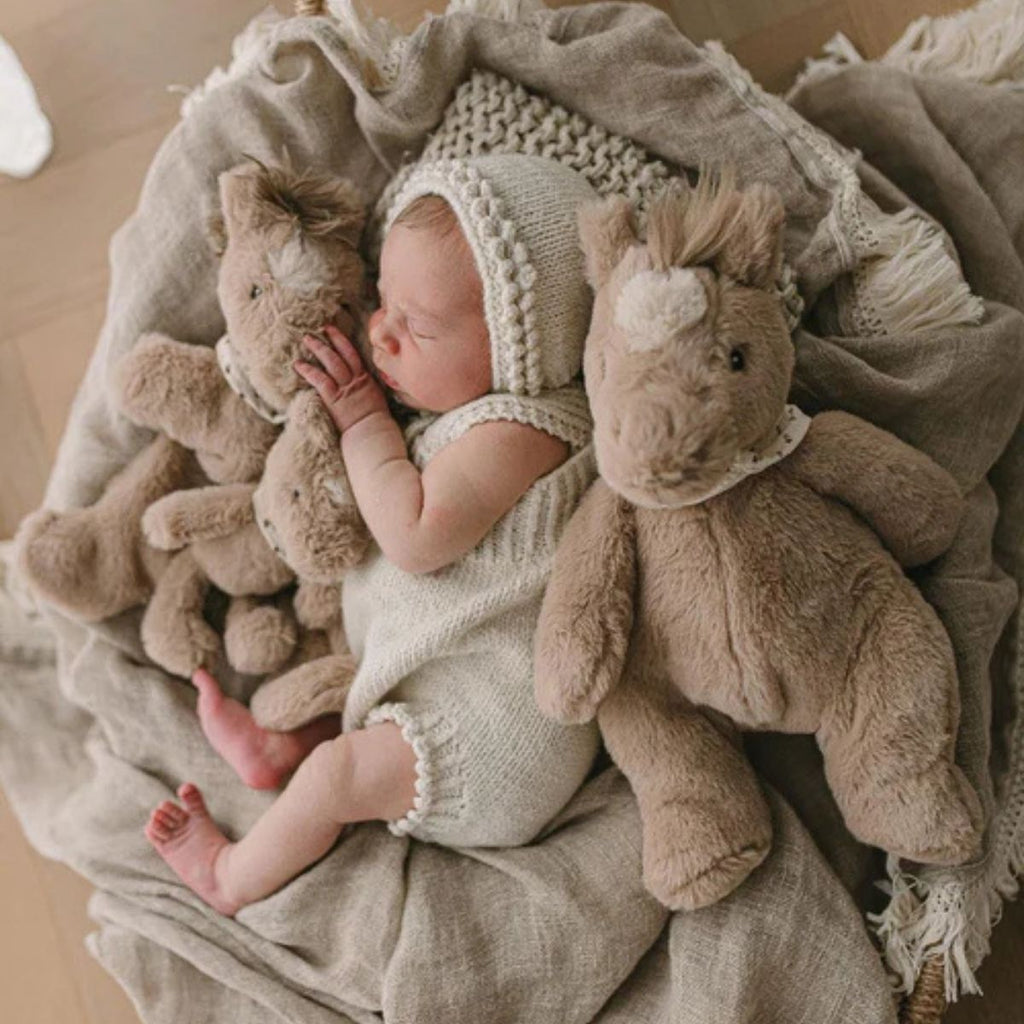 Newborn baby in a knitted outfit surrounded by plush toys on a soft blanket.