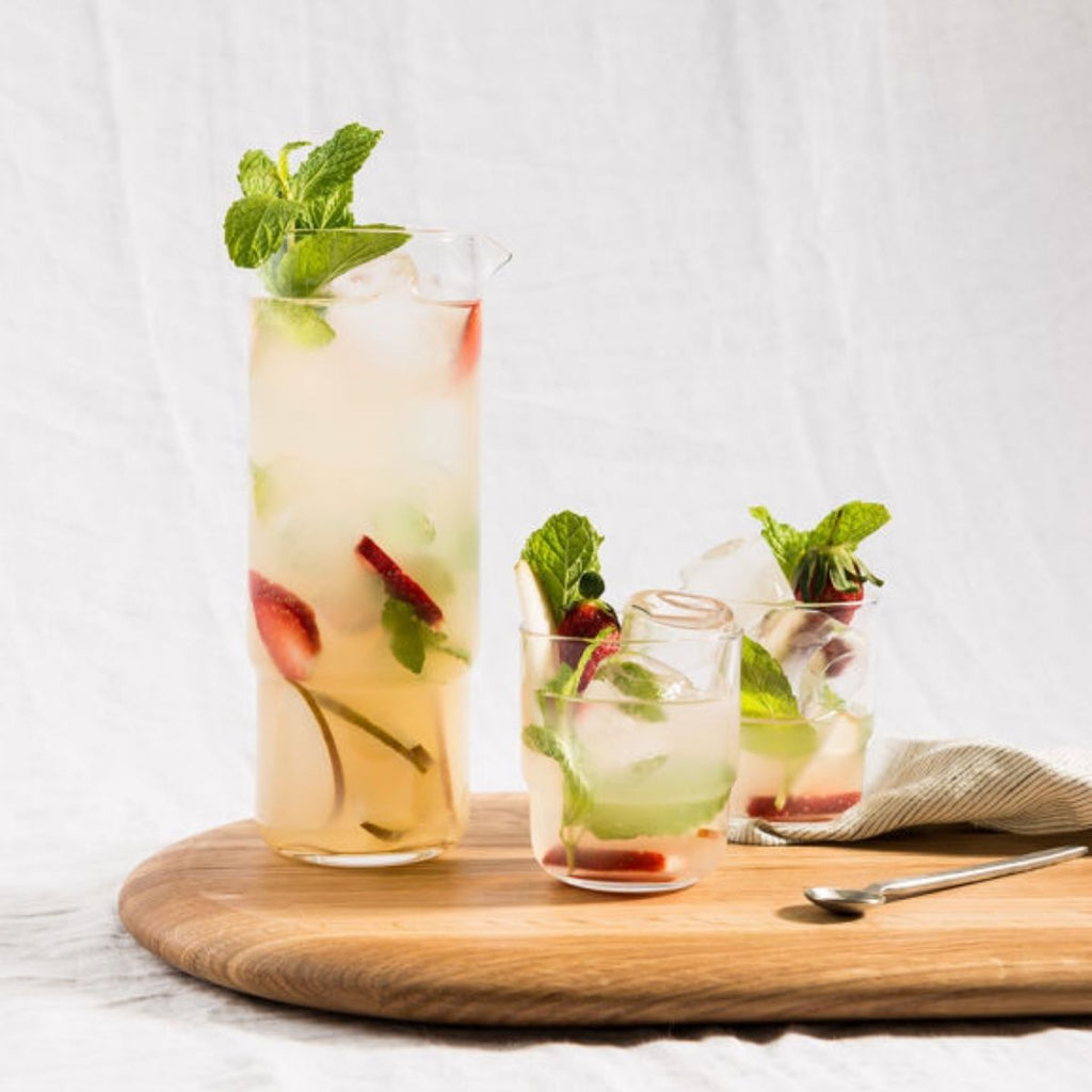 Three glasses of iced drinks with strawberries and mint leaves on a wooden board.
