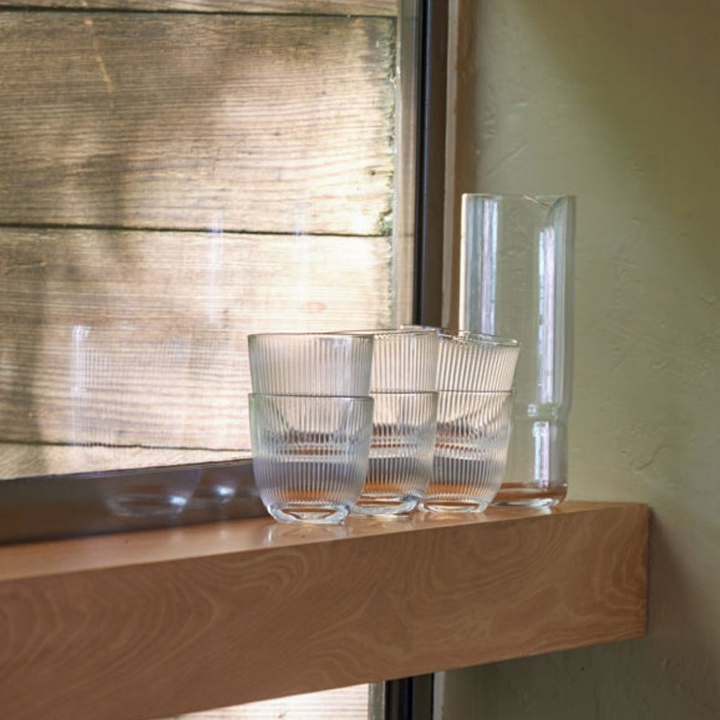 Clear glass bowls and a vase on a wooden surface with a window in the background
