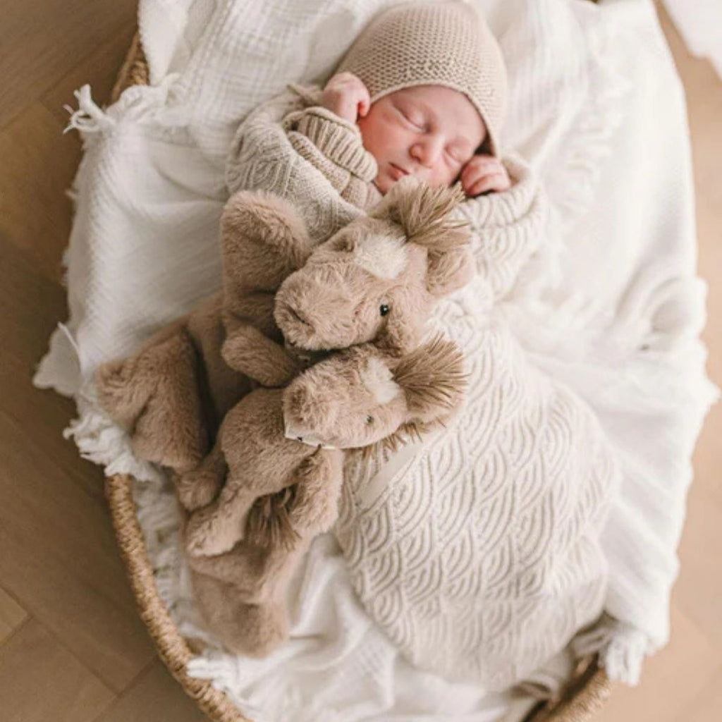 Plush toy horses next to a sleeping baby on a cream blanket