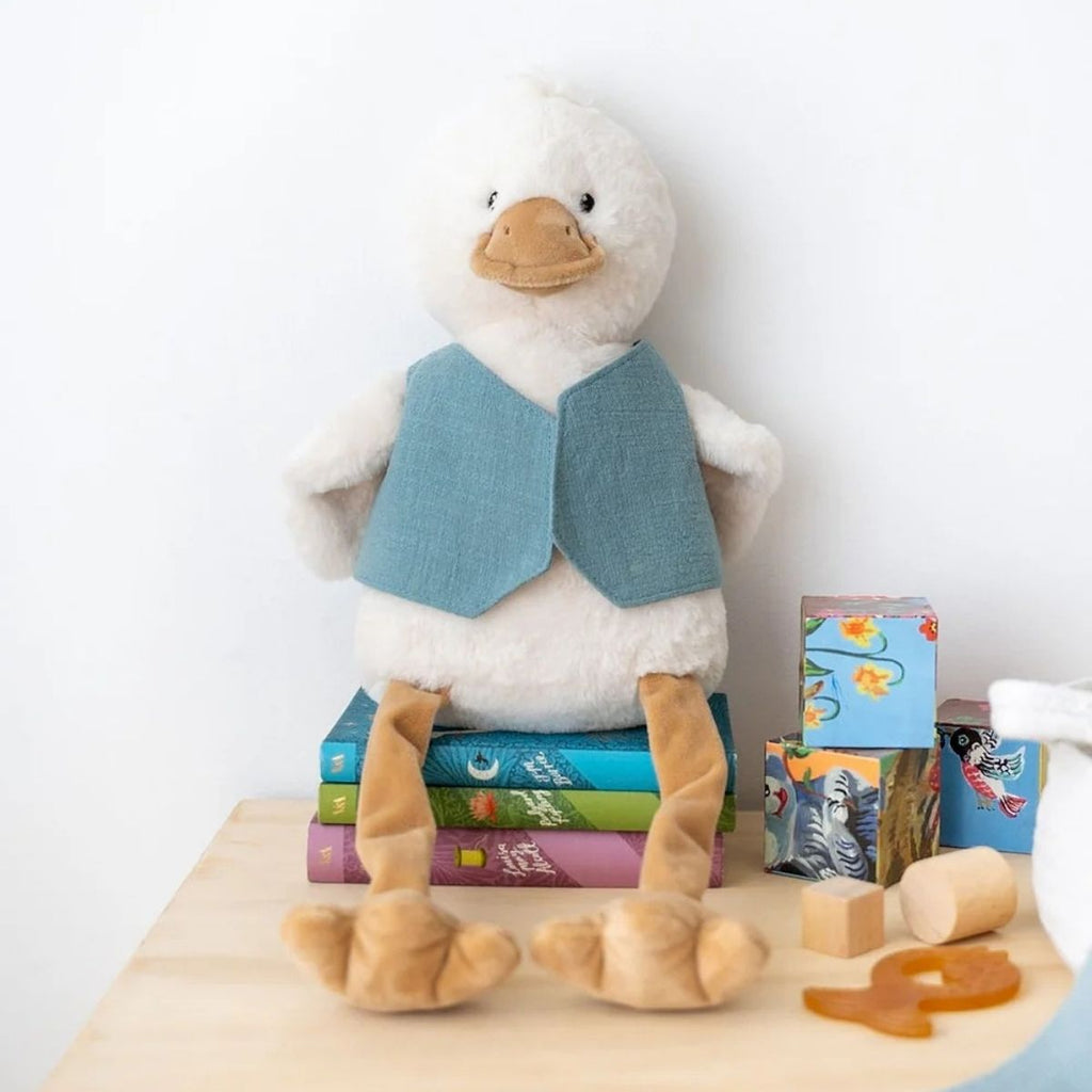Plush duck toy wearing a blue vest on top of children's books with a white background