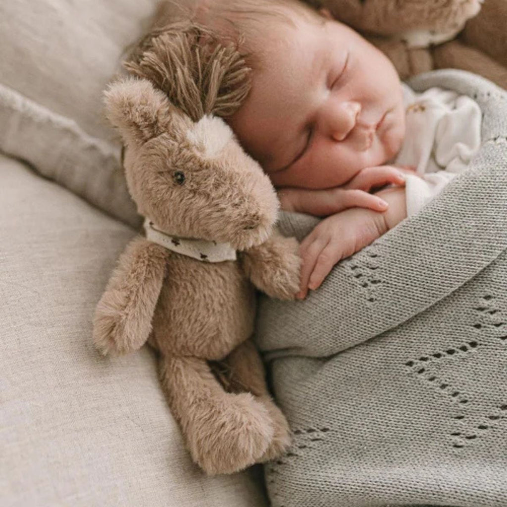 Plush toy horse next to a sleeping baby on neutral blankets
