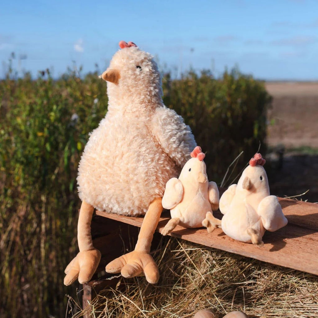 Large and small plush toy chickens on a wooden bench outdoors