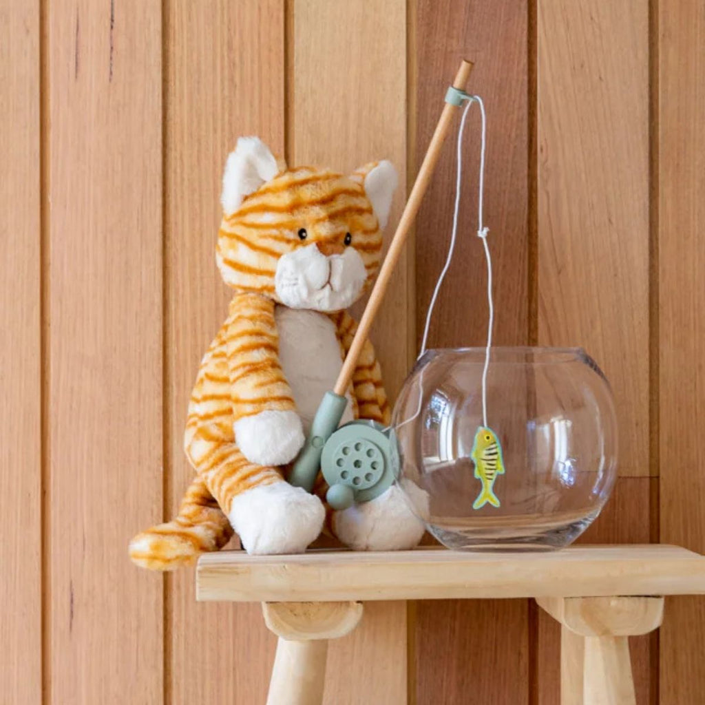 Plush tiger toy with fishing rod and glass bowl with fish toy on a wooden surface