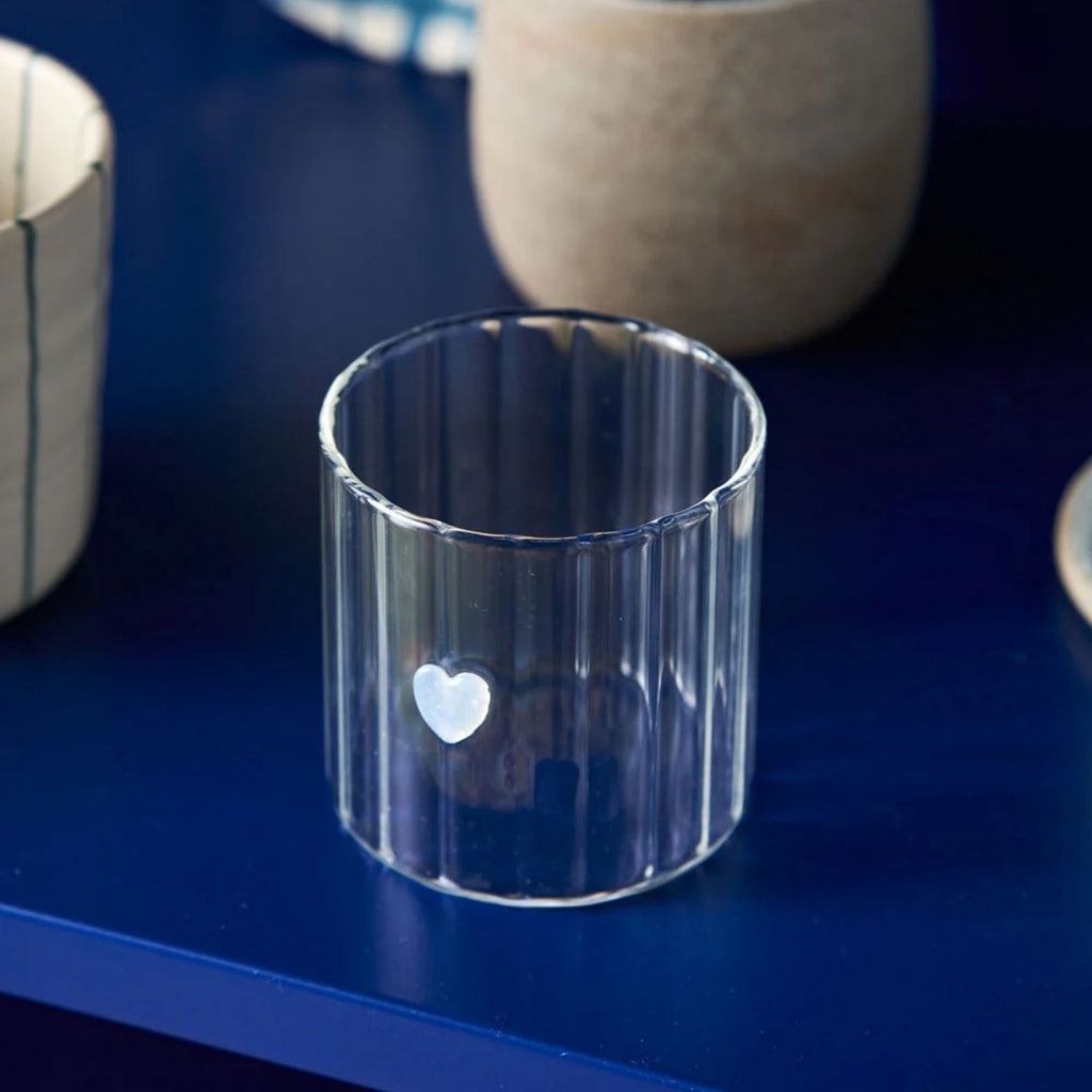 Clear glass candle holder with a heart design on a blue surface