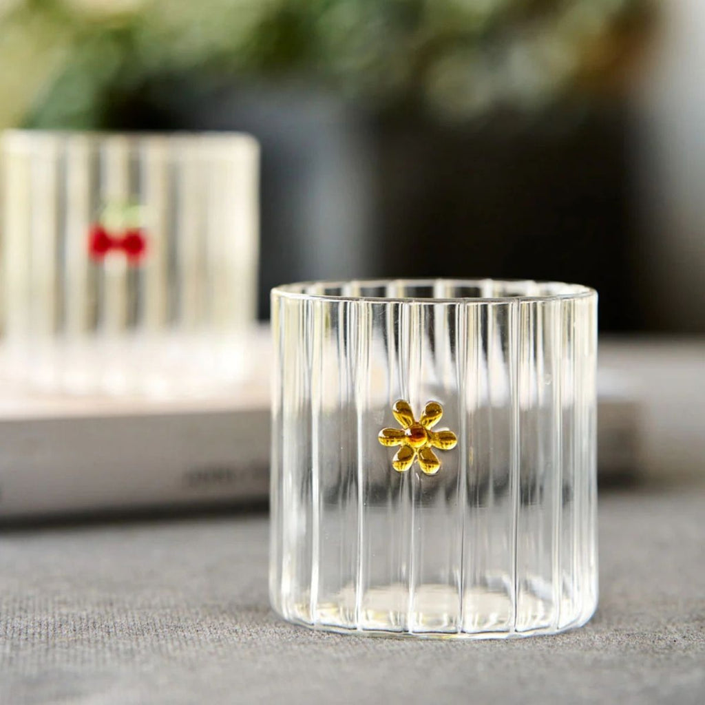 Clear glass candle holder with a gold flower detail on a surface.