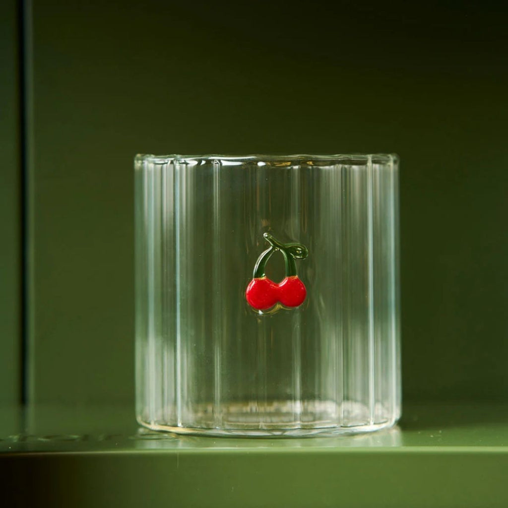 Clear glass with a cherry charm on a dark green background