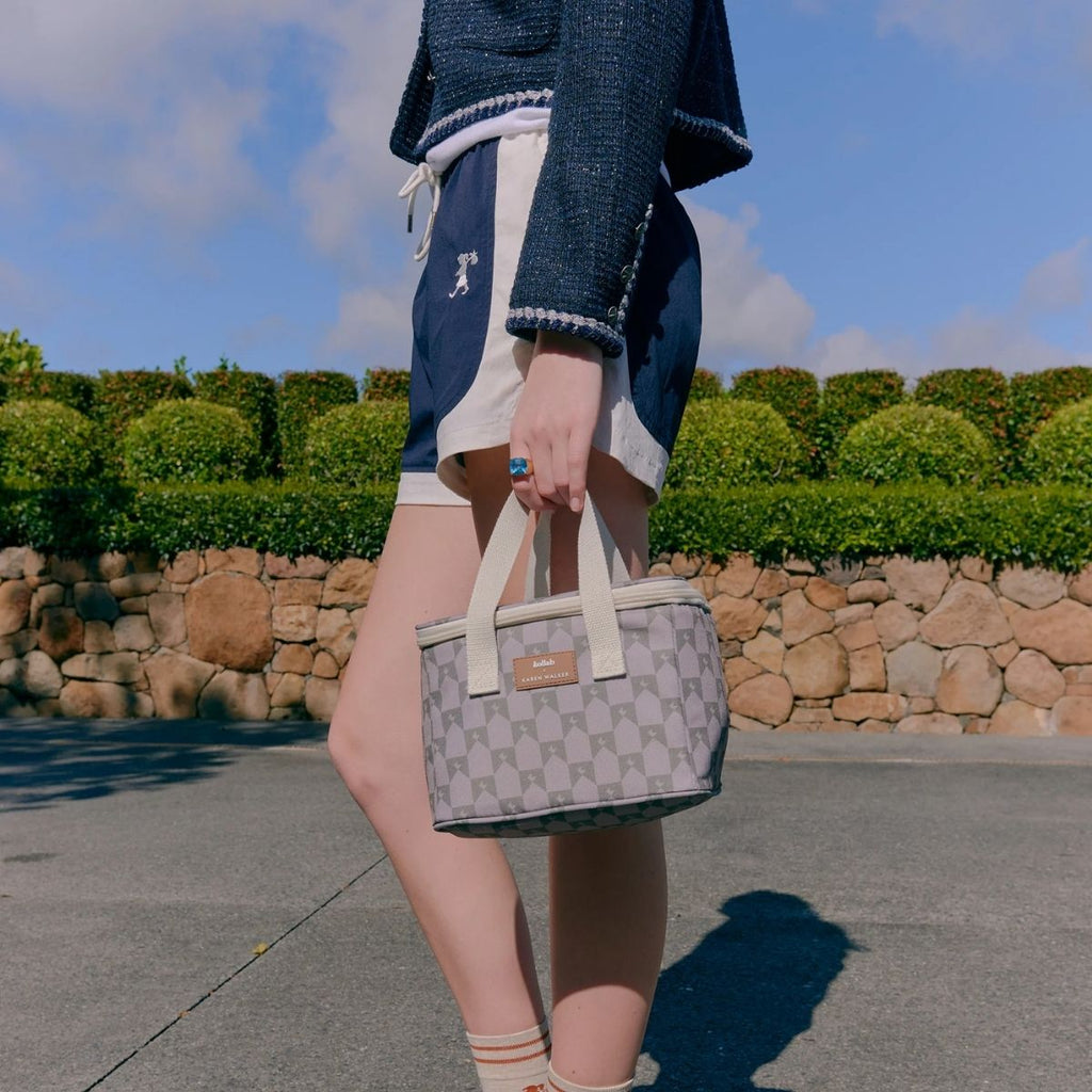 Person holding a patterned handbag outdoors with greenery and a stone wall in the background