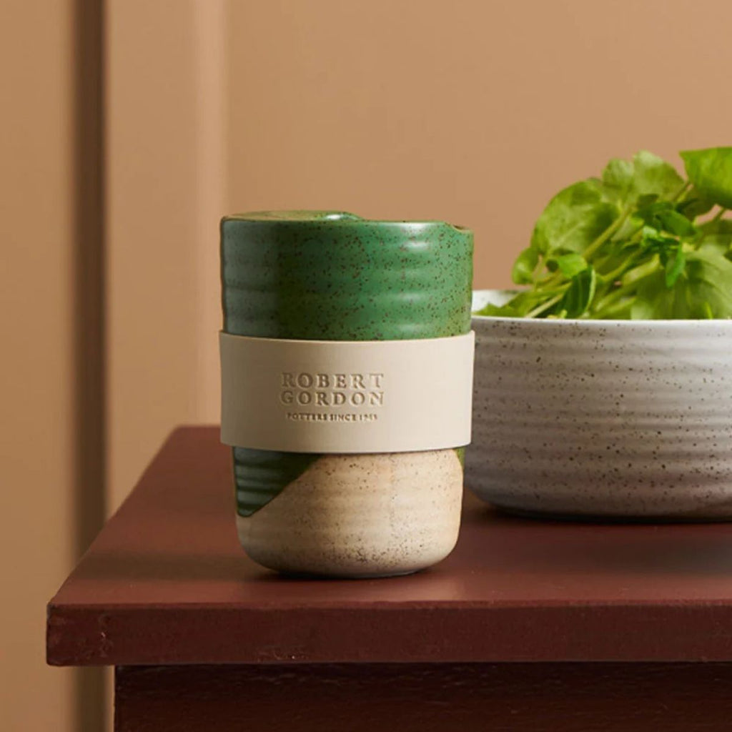 Green and beige ceramic cup with 'Robert Gordon' branding on a wooden surface.