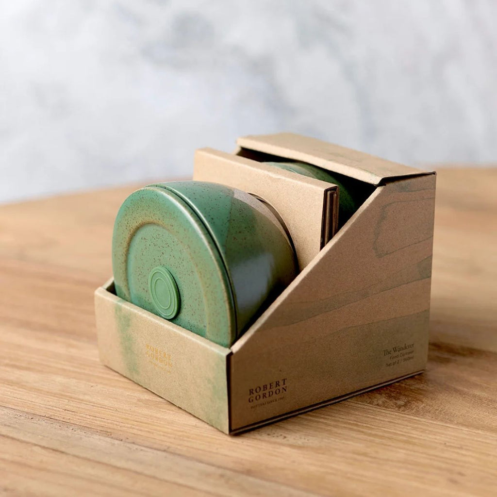 Green cylindrical container in a cardboard holder on a wooden surface with a blurred background