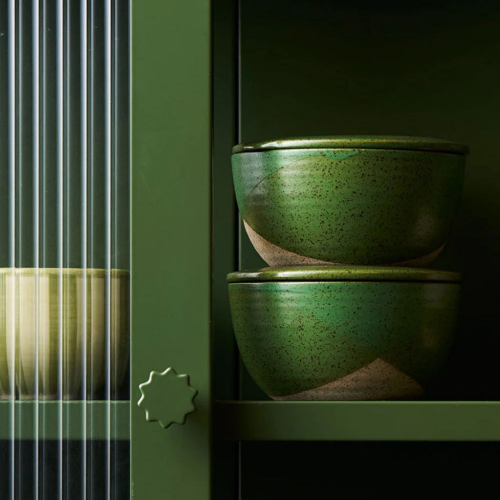 Two green ceramic bowls stacked on a dark green shelf.