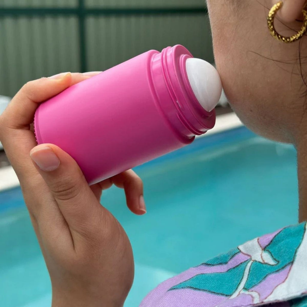 Person applying sunscreen with a pink bottle by a pool