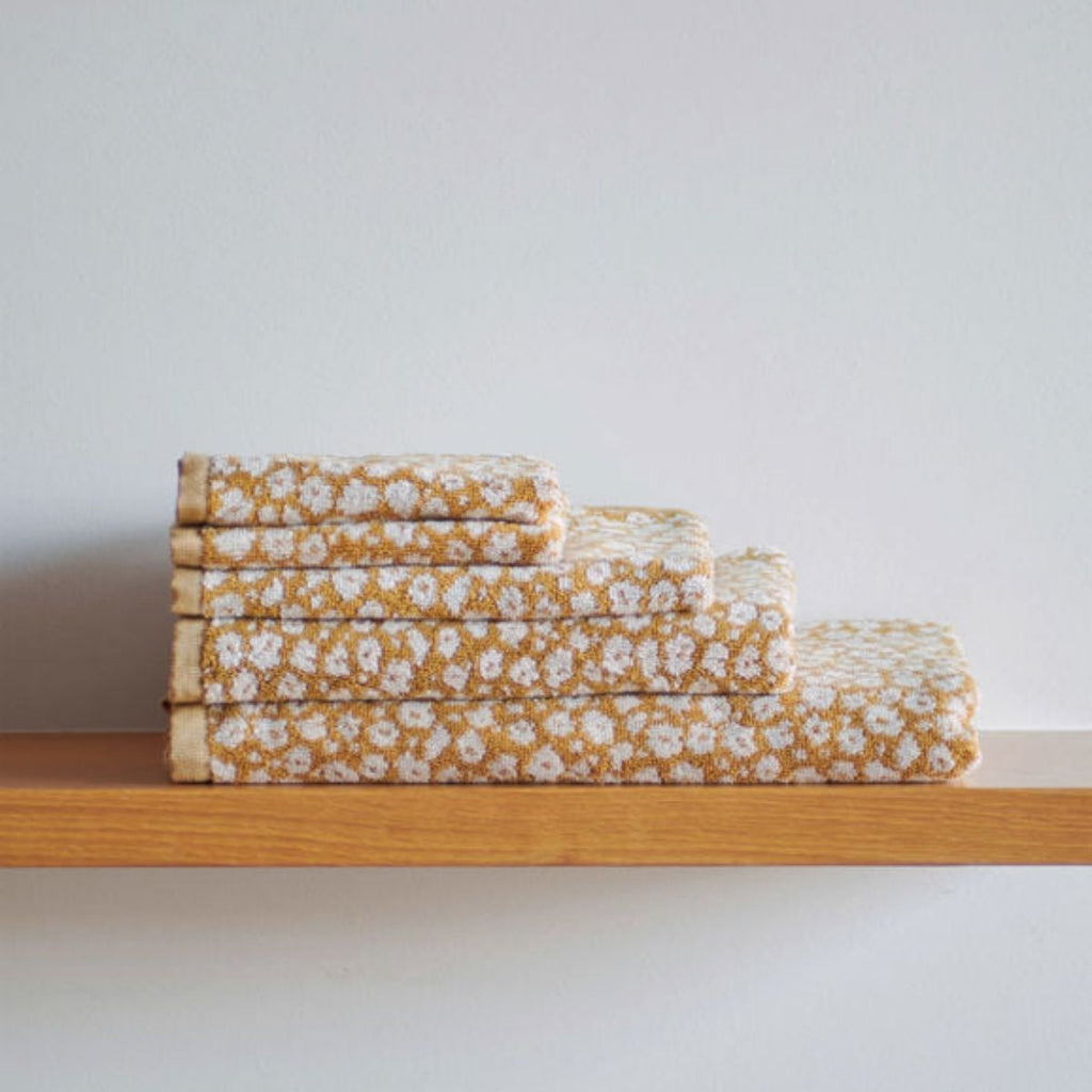 Stack of folded floral towels on a wooden shelf with a light gray background