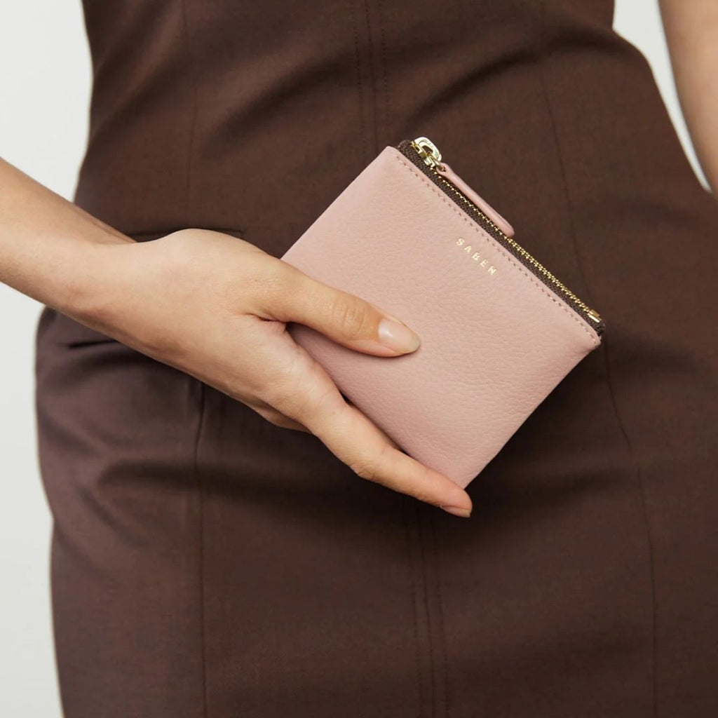 Person holding a pink wallet with a visible brand name against a neutral background