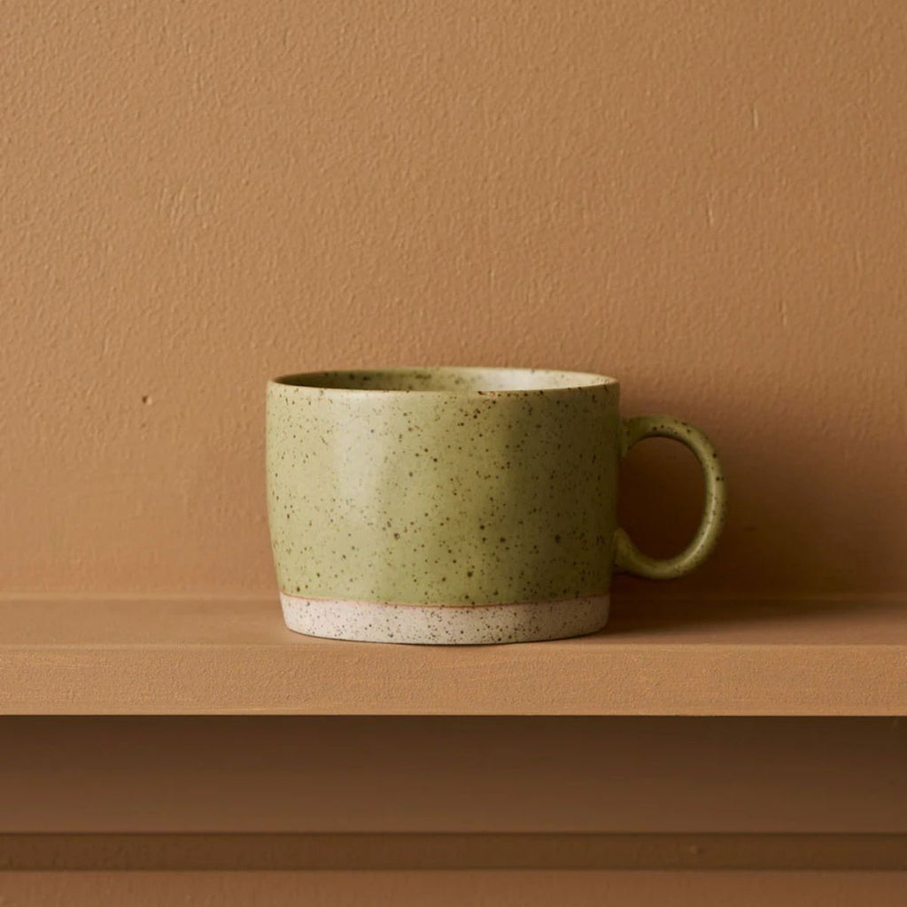 Green ceramic mug on a brown surface with a matching brown wall background