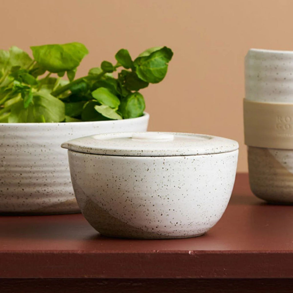 Speckled ceramic bowl with a lid on a wooden surface, with a beige wall in the background.