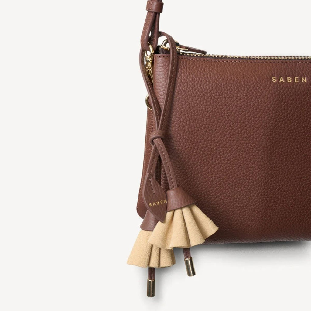 Brown leather handbag with tassel detail on a white background