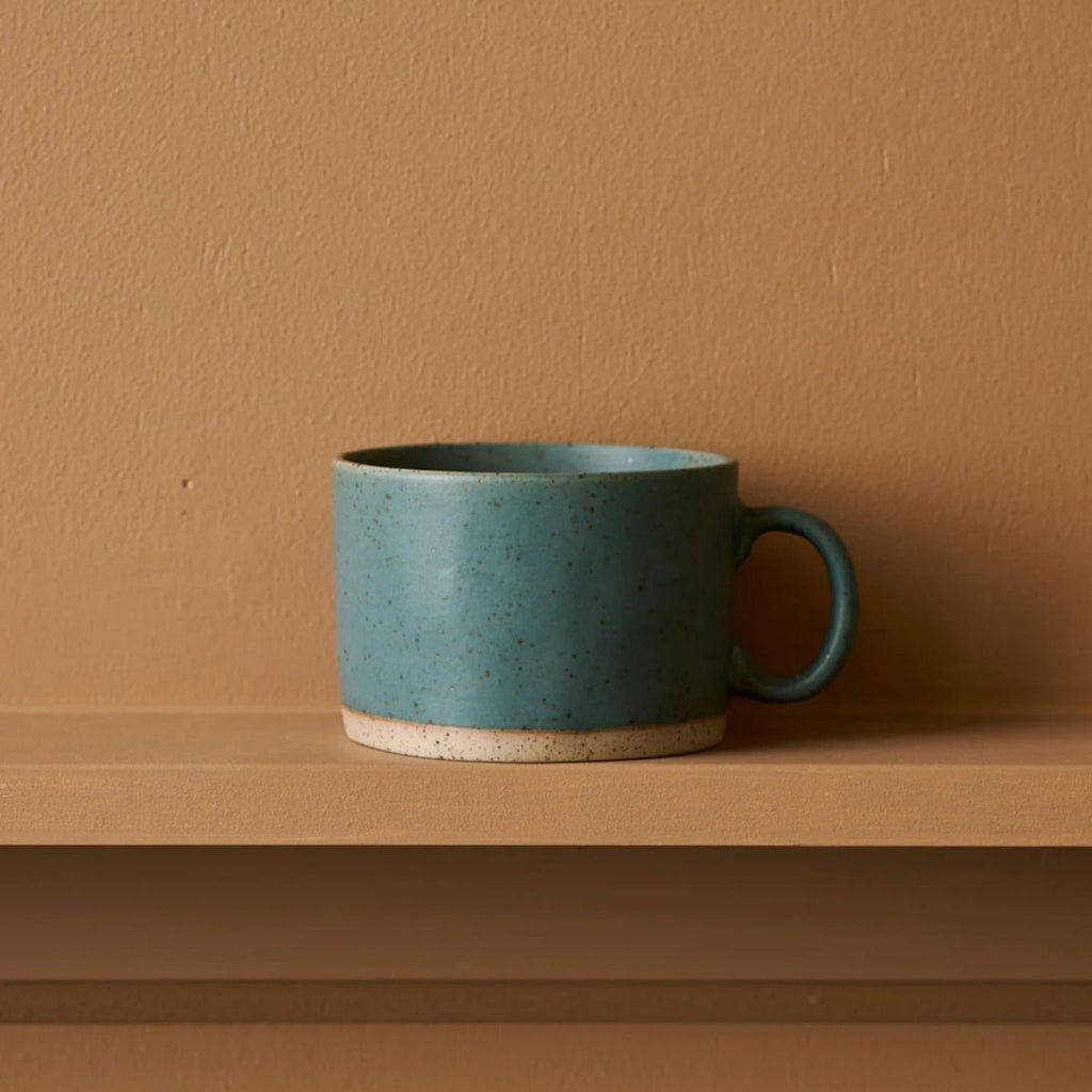 Blue ceramic mug on a wooden shelf against a brown wall