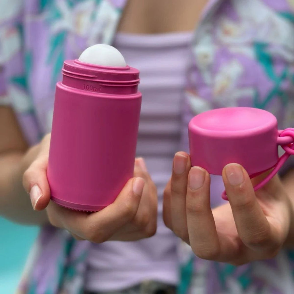Person holding two pink containers, one larger and one smaller, with a blurred background.
