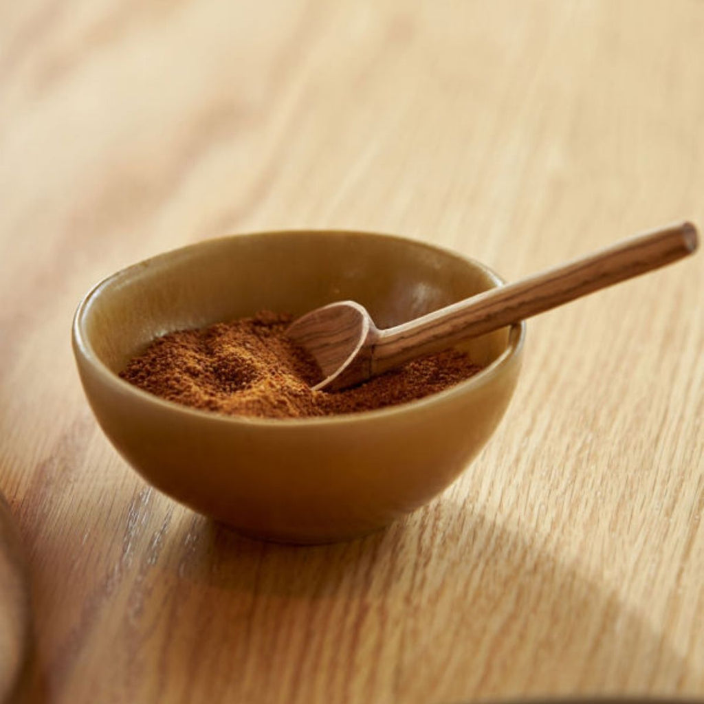 Brown bowl with ground spice and wooden spoon on a wooden surface