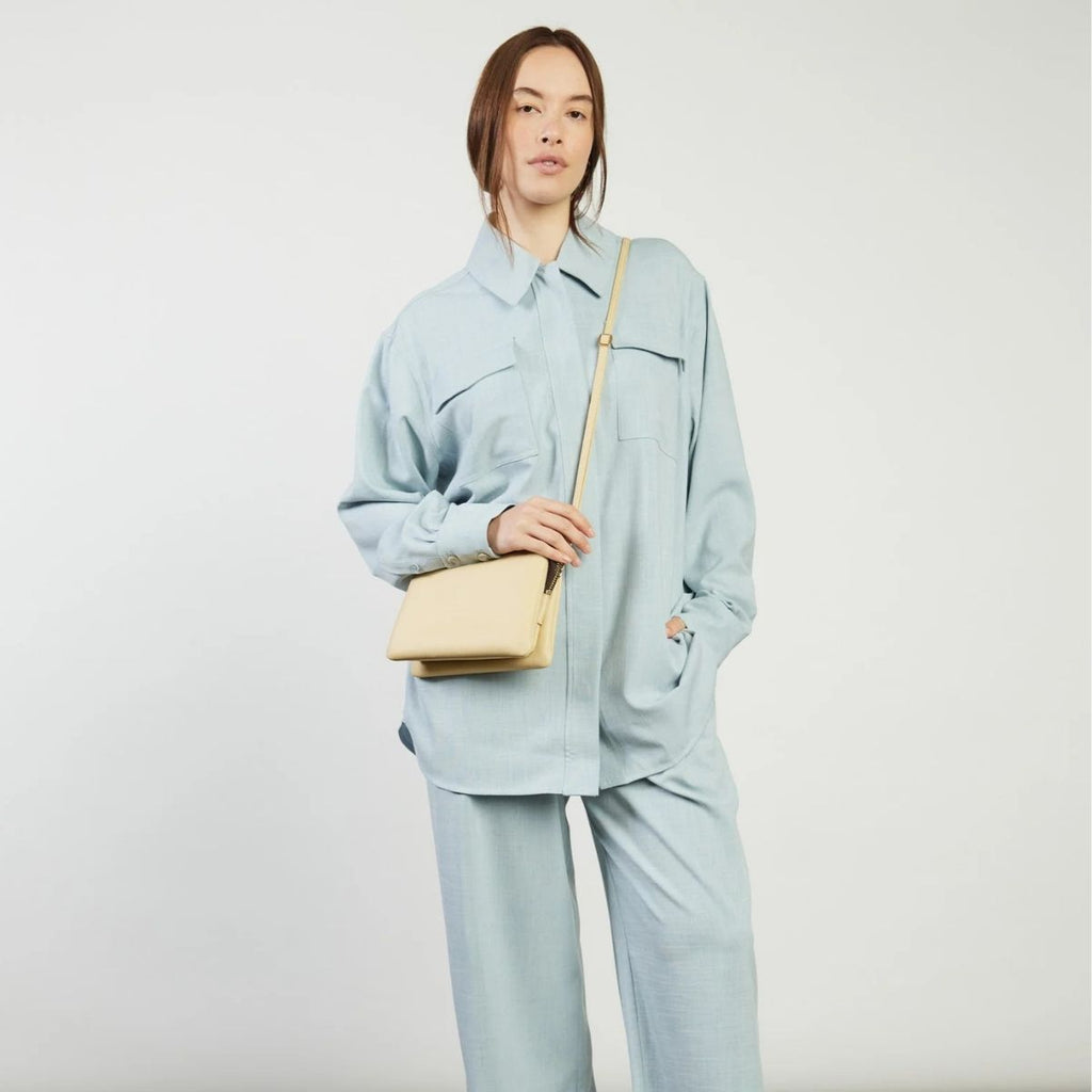 Person wearing a light blue outfit with a beige bag on a plain background