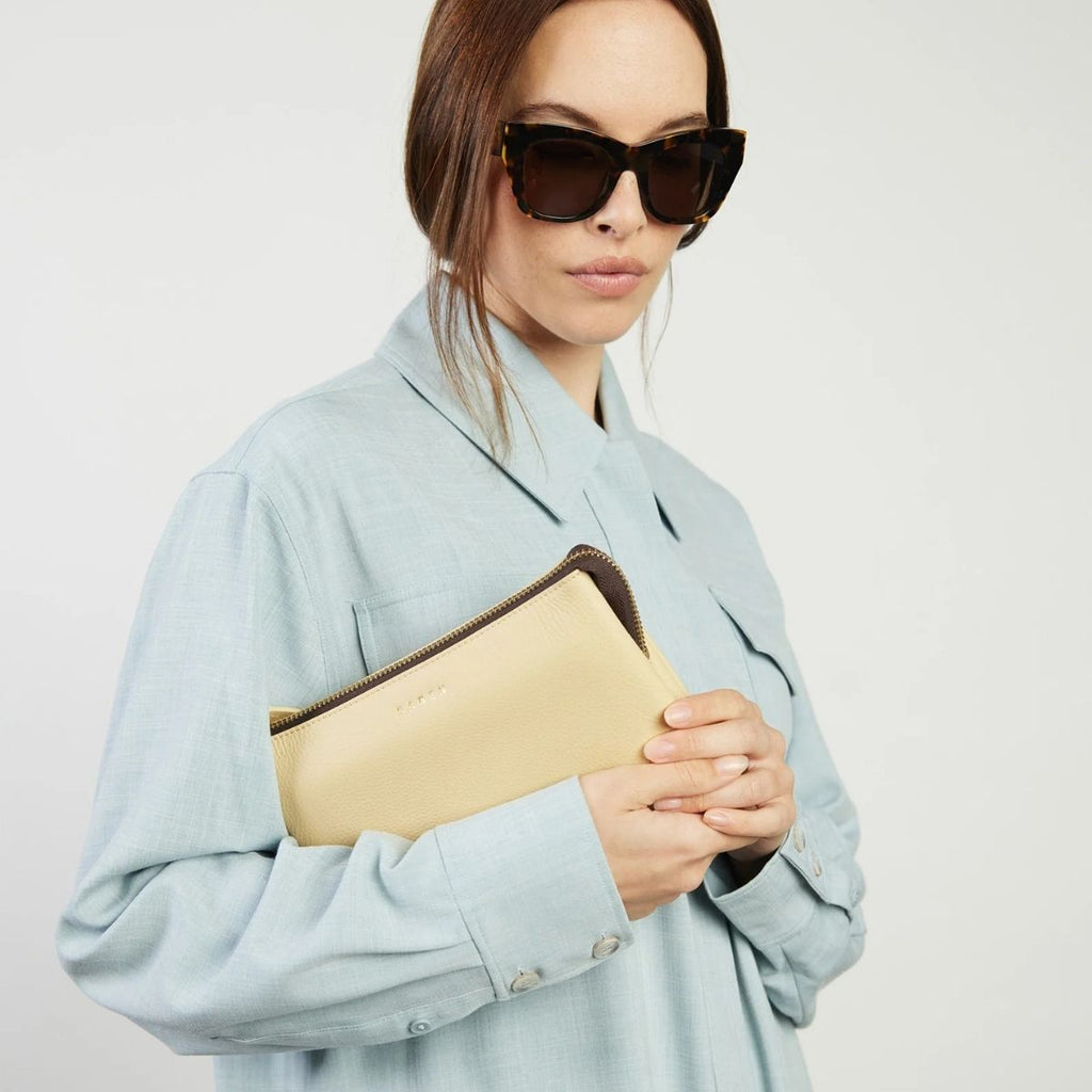 Woman holding a beige clutch with a light gray background