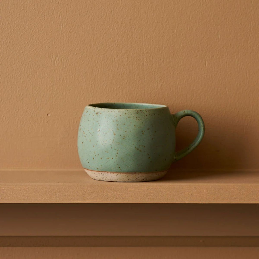 Green ceramic mug on a wooden shelf with a brown background