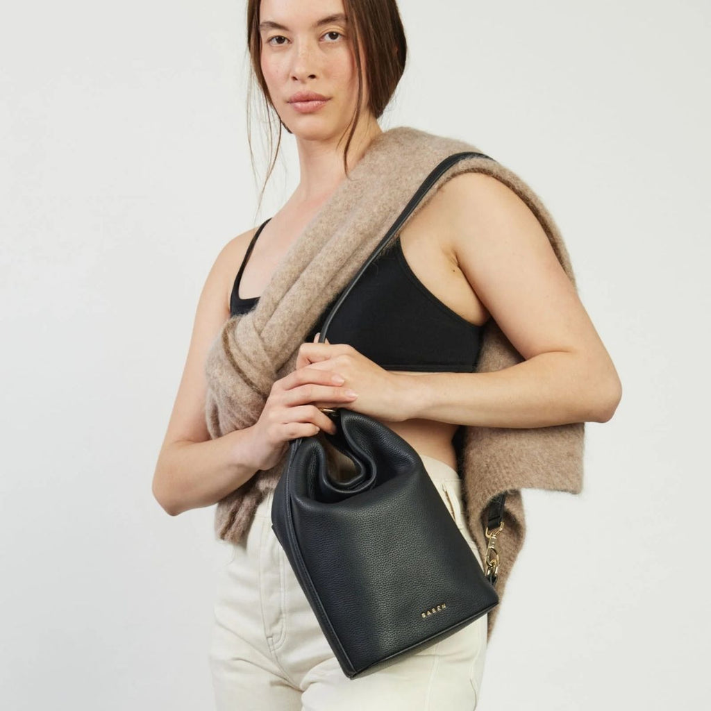 Woman holding a black handbag against a plain background