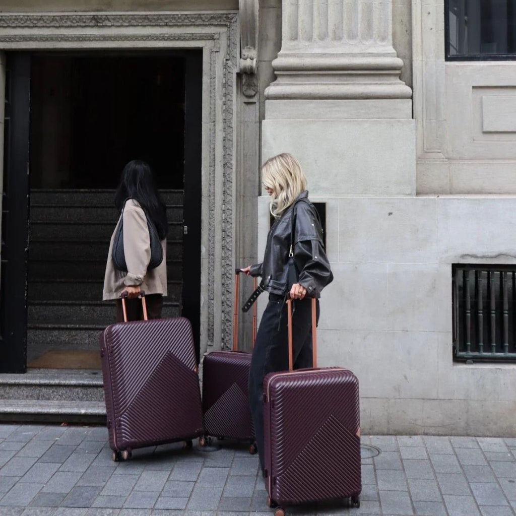 Two women wheeling suitcases into a building.