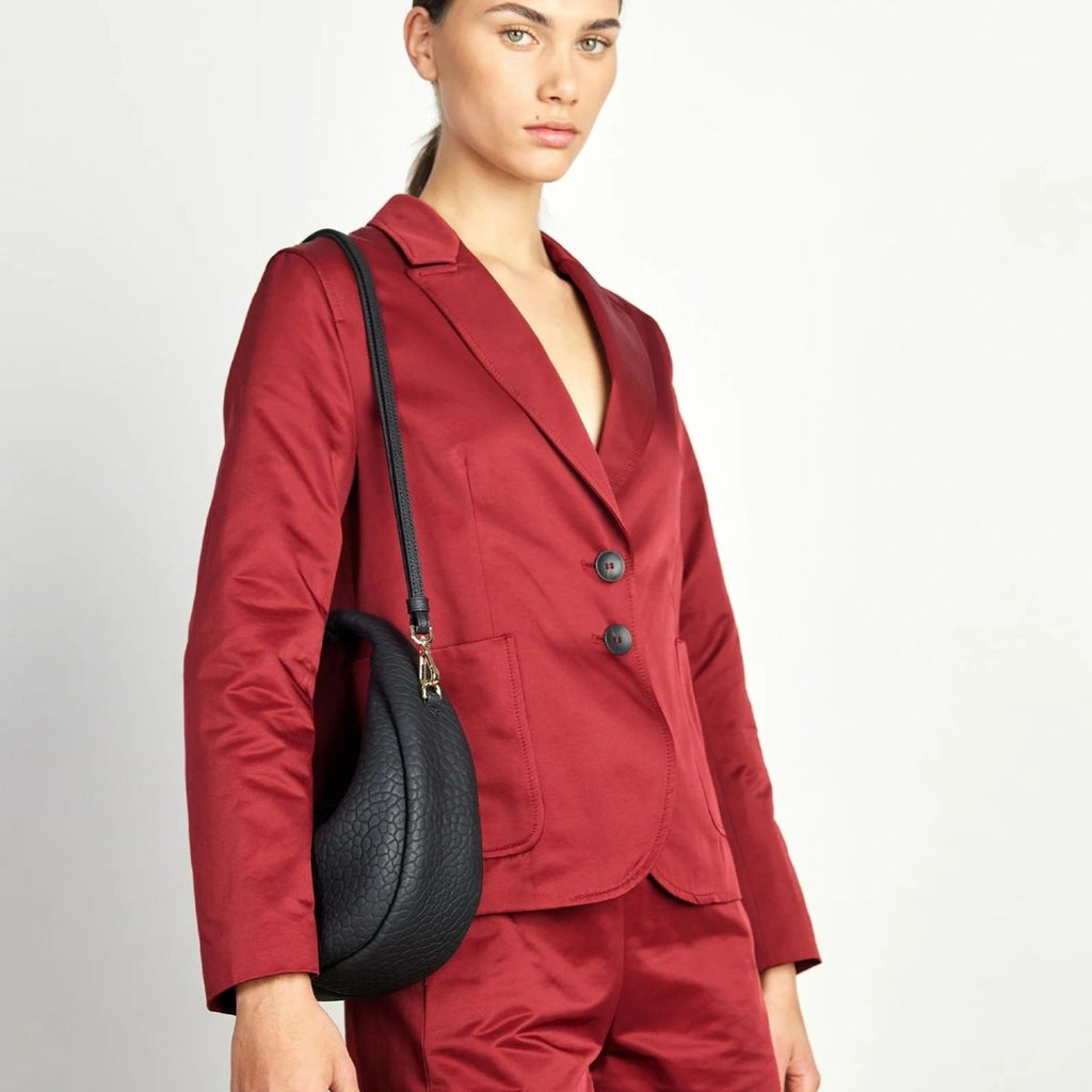 Woman wearing a red suit with a black handbag on a plain background