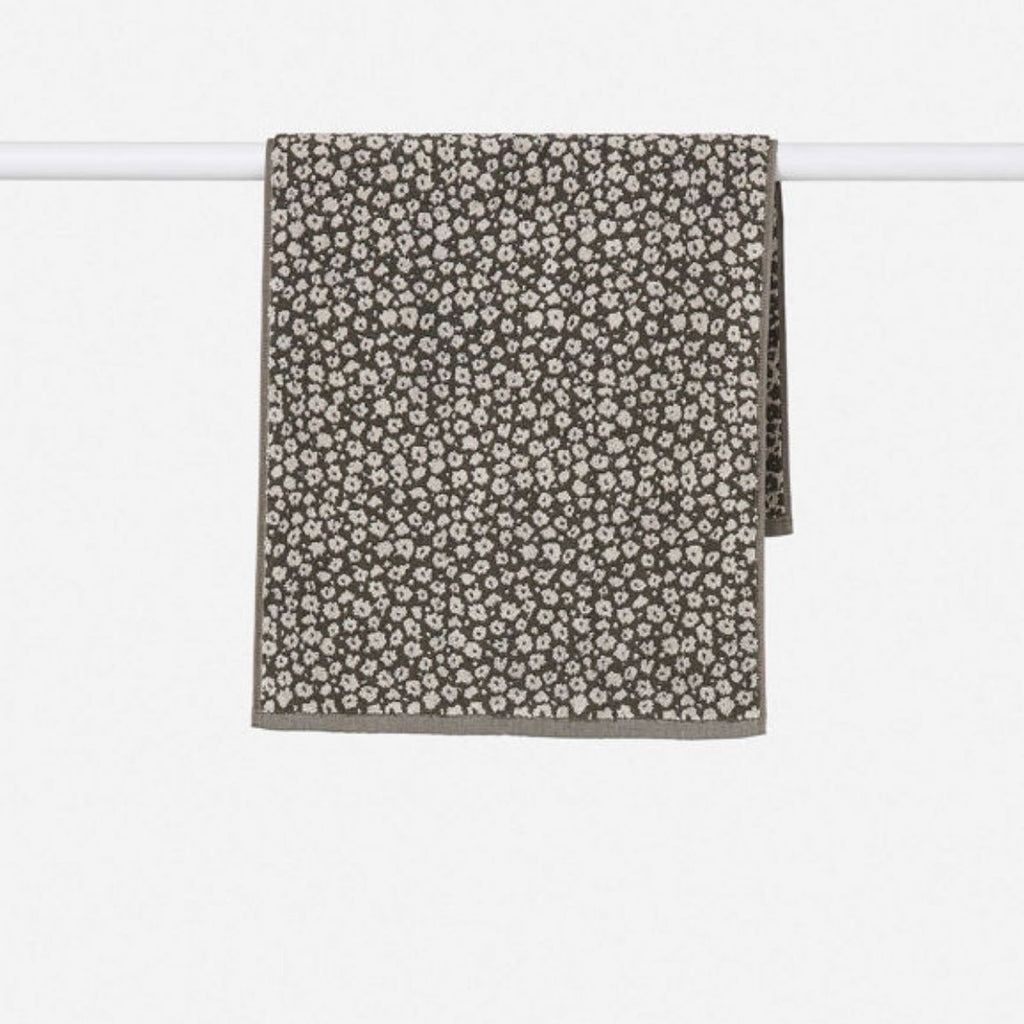 Floral patterned towel hanging on a white rod against a white background