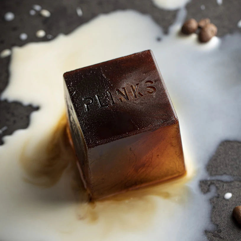 Cube of coffee with 'PLINKS' branding on a dark surface with milk.